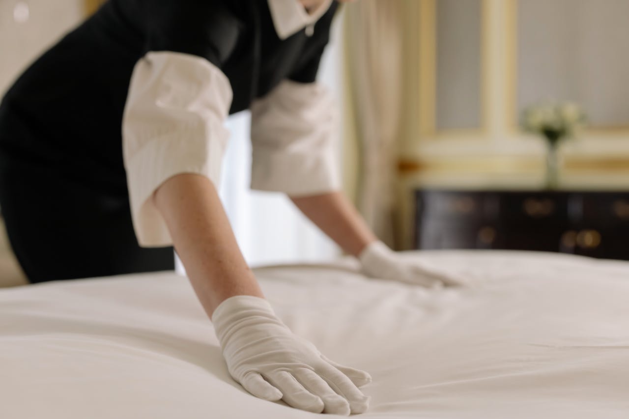 A housekeeper straightening the bed linens in a well-appointed hotel room.